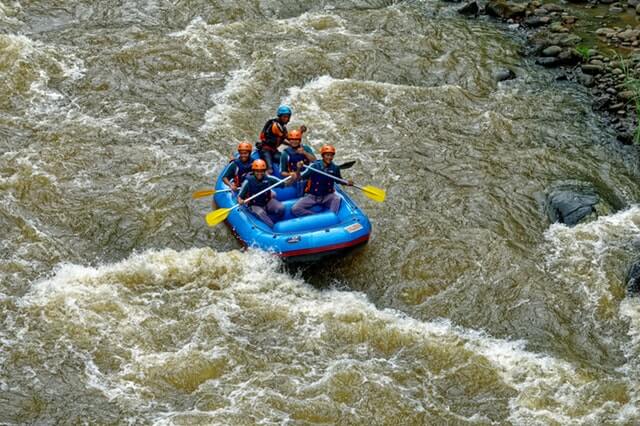 A imagem mostra 5 pessoas em um bote praticando rafting