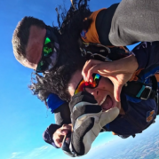 Instrutor de paraquedismo e aluno em queda livre durante salto de paraquedas, exemplo de esporte em grupo.