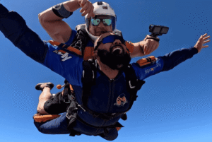 Instrutor de paraquedismo e aluno em queda livre durante salto duplo de paraquedas.