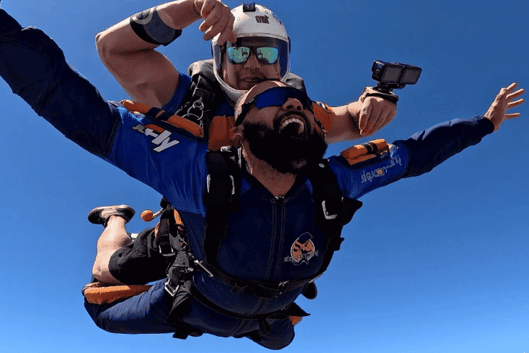 Instrutor de paraquedismo e aluno em queda livre durante salto duplo de paraquedas.