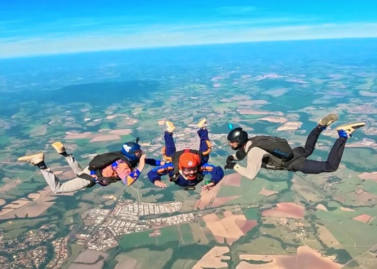 Dois instrutores de paraquedismo acompanhando um aluno em queda livre após saltar de paraquedas sozinho