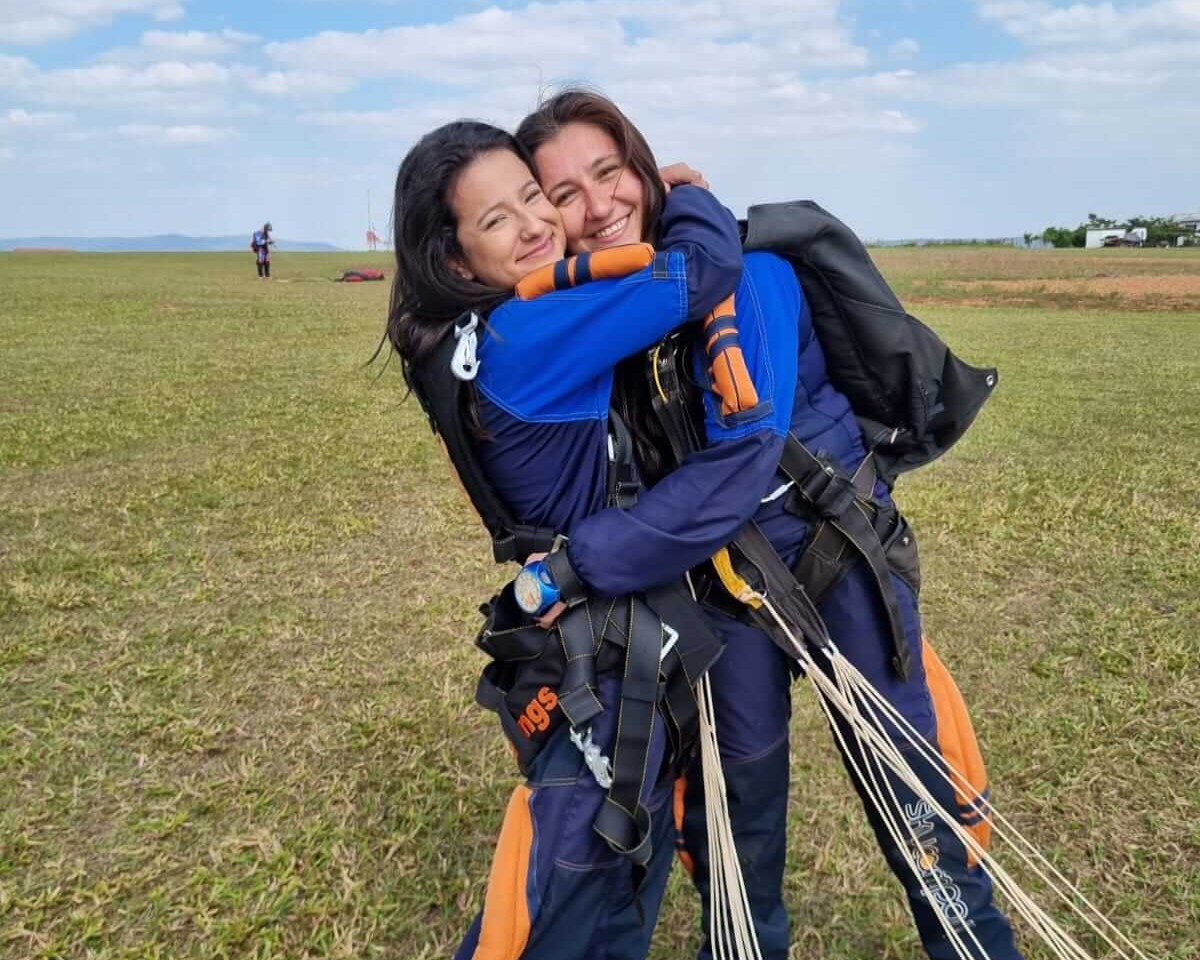 Casal de mulheres abraçadas em solo após salto de paraquedas.
